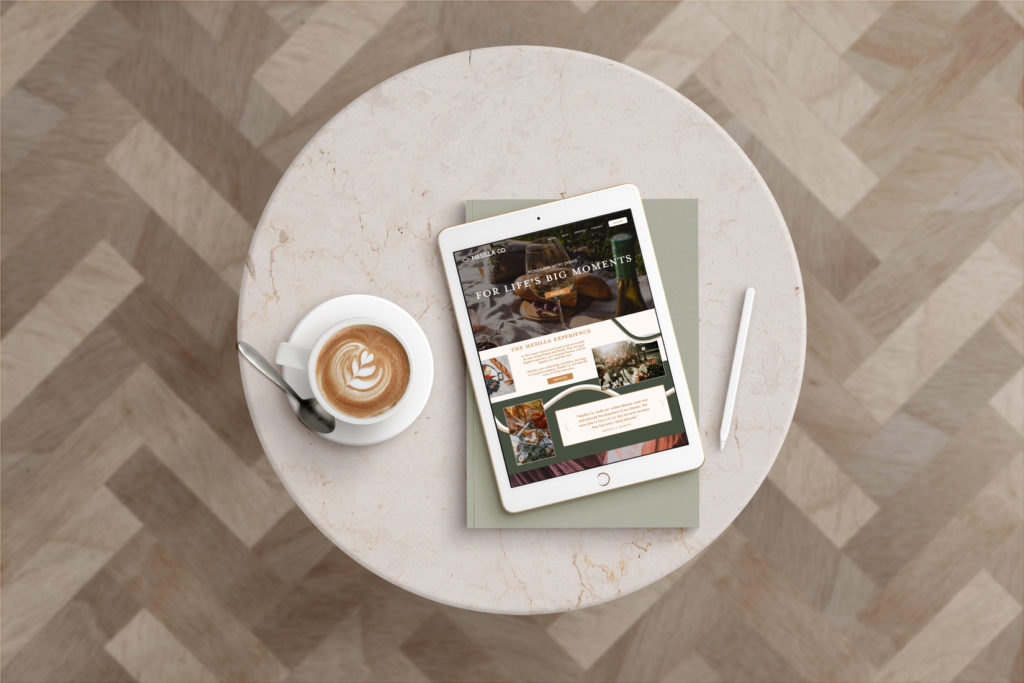 A mock-up of the home page of a website design for Mesilla Co. a picnic and micro event company. The homepage is on an iPad screen on a marble table with a cup of coffee and a book designed by Kin & Co. Design Studio a strategic brand and website designer.